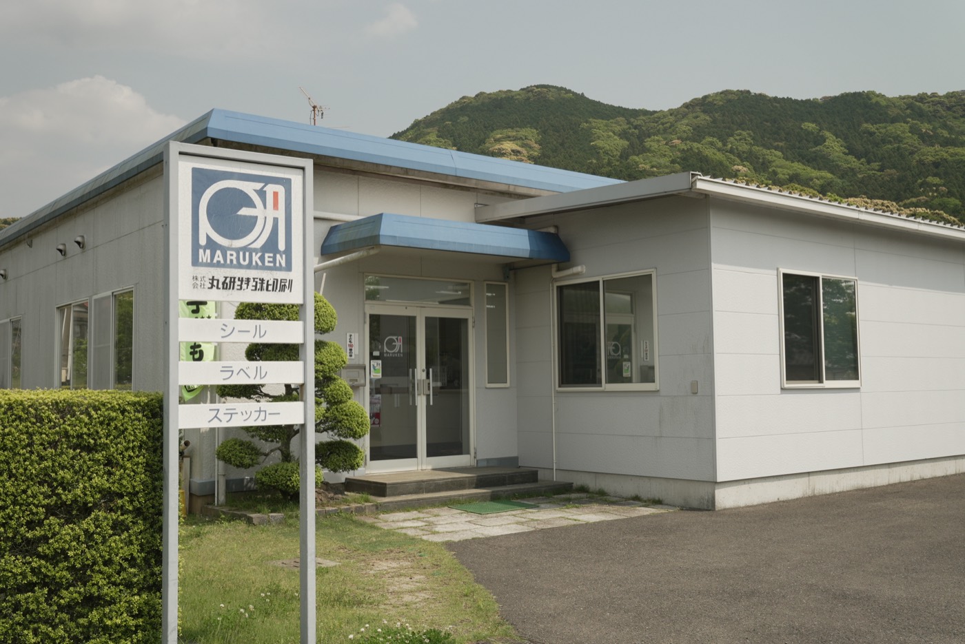 山を背にした丸研特殊印刷の社屋と看板